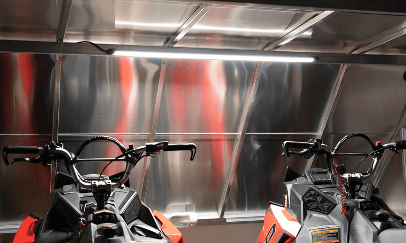 Kingpin v-Series 40" light bar illuminating two Polaris mountain snowmobiles inside enclosed aluminum trailer.